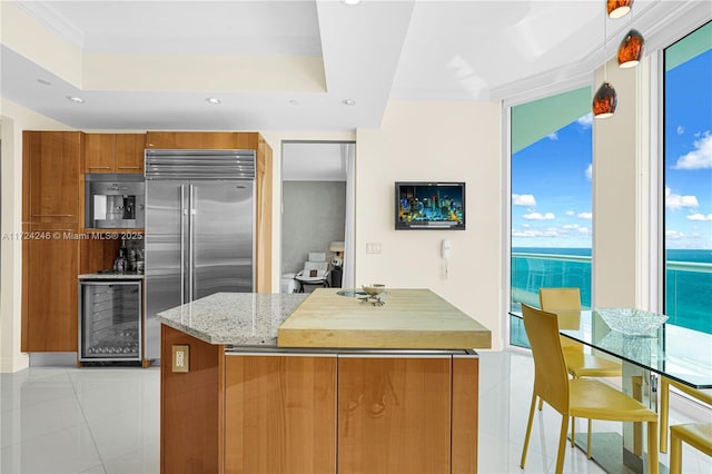 kitchen with built in fridge, wine cooler, a water view, light stone counters, and crown molding