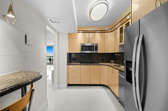 kitchen with decorative backsplash, light brown cabinetry, dark stone counters, stainless steel appliances, and light tile patterned floors