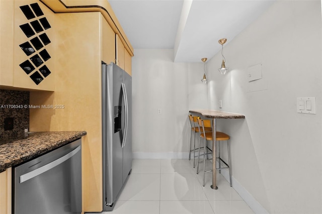 kitchen with dark stone counters, hanging light fixtures, light tile patterned floors, light brown cabinetry, and appliances with stainless steel finishes