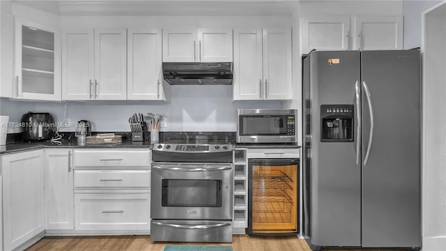 kitchen featuring dark stone counters, appliances with stainless steel finishes, light wood-type flooring, and white cabinetry