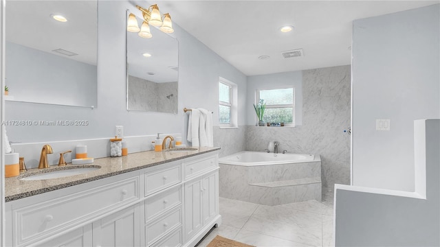 bathroom with tile patterned flooring, tiled tub, and vanity