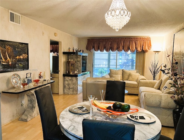 dining space featuring an inviting chandelier, a textured ceiling, and light wood-type flooring