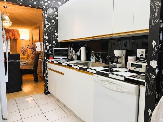 kitchen with dishwasher, light tile patterned flooring, white cabinetry, and sink