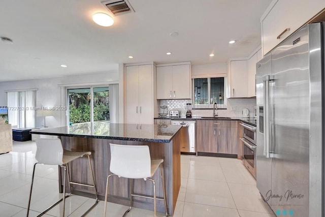 kitchen featuring white cabinets, sink, decorative backsplash, dark stone countertops, and appliances with stainless steel finishes