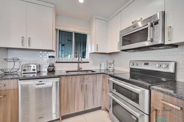 kitchen with sink, tasteful backsplash, dark stone counters, light tile patterned floors, and appliances with stainless steel finishes