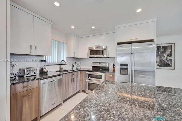 kitchen with stainless steel appliances, white cabinetry, dark stone counters, and sink