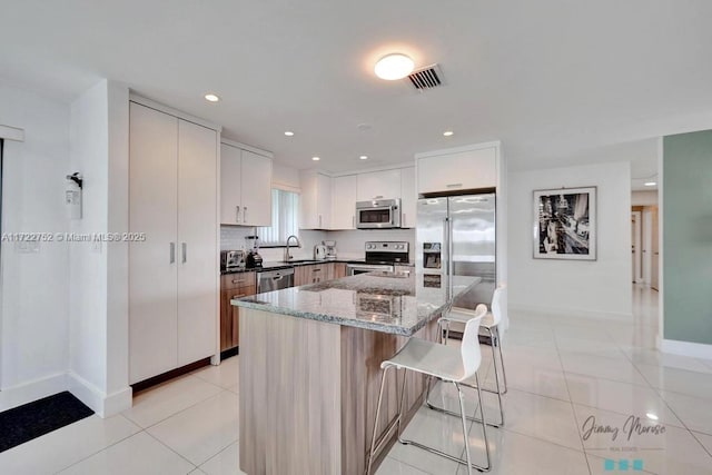 kitchen featuring a center island, light tile patterned flooring, a breakfast bar area, white cabinets, and appliances with stainless steel finishes