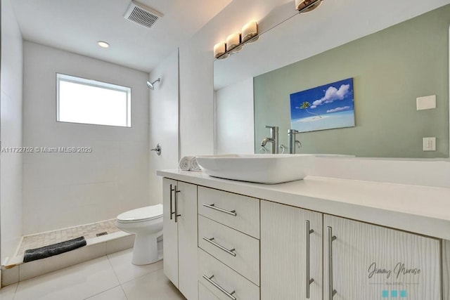 bathroom with tile patterned flooring, vanity, toilet, and tiled shower