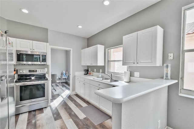 kitchen with appliances with stainless steel finishes, hardwood / wood-style floors, white cabinetry, sink, and kitchen peninsula