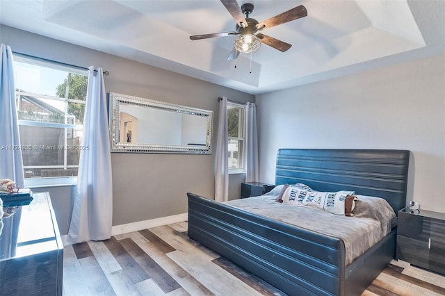 bedroom featuring ceiling fan, wood-type flooring, and a raised ceiling