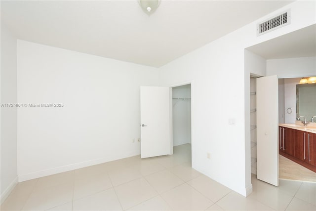 unfurnished bedroom with a walk in closet, ensuite bathroom, a closet, and light tile patterned flooring