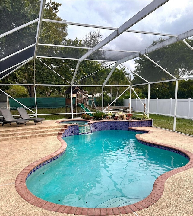 view of pool with a playground, an in ground hot tub, glass enclosure, and a patio