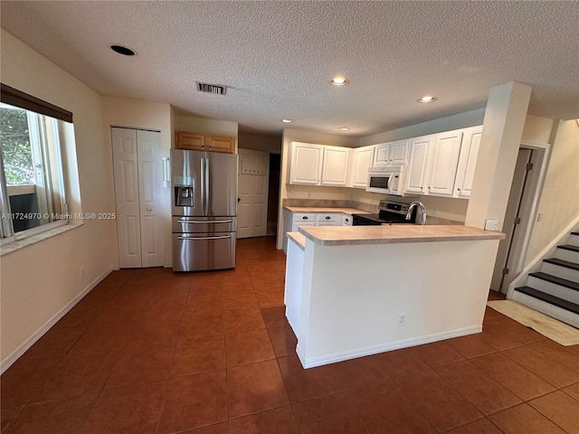 kitchen with white cabinetry, stainless steel appliances, a textured ceiling, dark tile patterned flooring, and kitchen peninsula