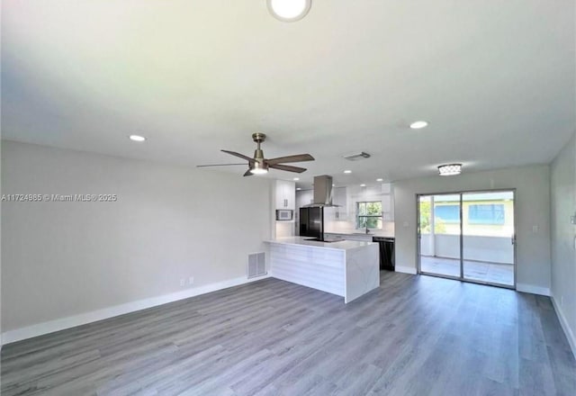 kitchen with dishwasher, kitchen peninsula, white cabinetry, wood-type flooring, and island exhaust hood