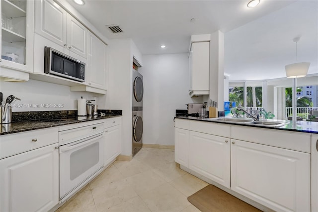 kitchen with sink, oven, stacked washer / dryer, and white cabinets