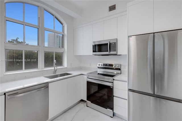 kitchen with light countertops, visible vents, appliances with stainless steel finishes, white cabinets, and a sink