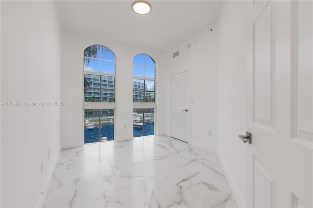 unfurnished room with marble finish floor, a high ceiling, a water view, and baseboards