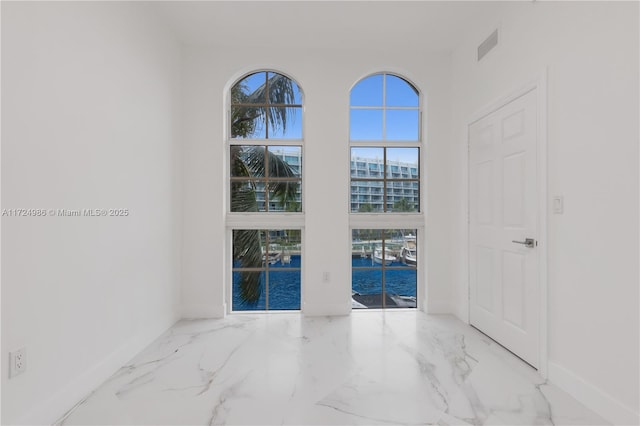 spare room featuring a water view, marble finish floor, and baseboards