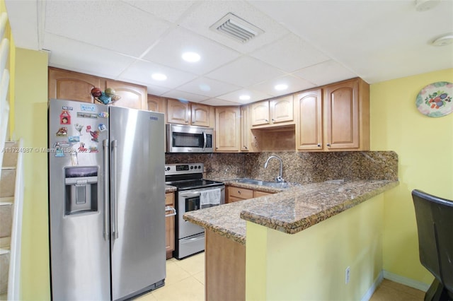 kitchen featuring sink, a drop ceiling, dark stone countertops, light tile patterned floors, and appliances with stainless steel finishes