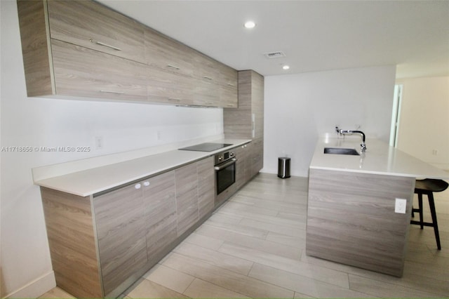 kitchen featuring a breakfast bar area, black electric cooktop, stainless steel oven, and sink