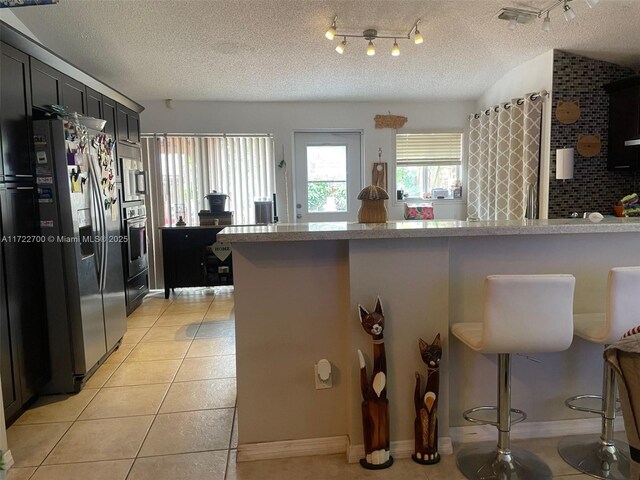 kitchen featuring stainless steel appliances, light tile patterned floors, a textured ceiling, a kitchen bar, and decorative backsplash