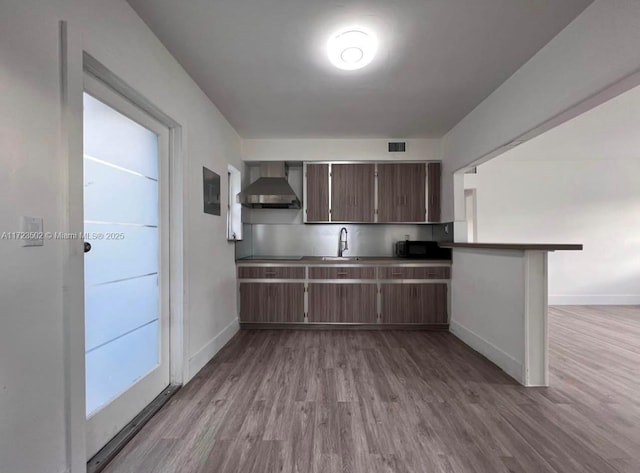 kitchen featuring sink, light hardwood / wood-style flooring, wall chimney exhaust hood, dark brown cabinets, and kitchen peninsula