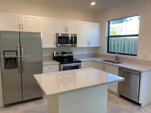 kitchen featuring light stone counters, stainless steel appliances, sink, white cabinets, and a center island