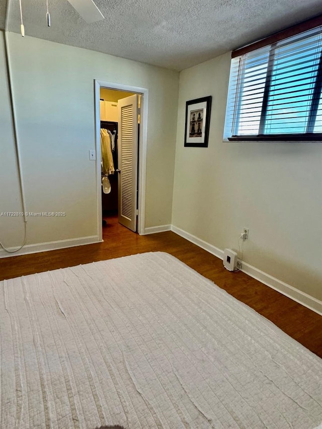 unfurnished bedroom with wood-type flooring, a walk in closet, a textured ceiling, and a closet