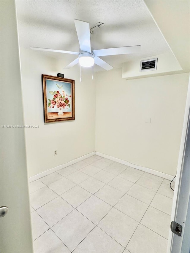 empty room featuring a textured ceiling, ceiling fan, and light tile patterned flooring