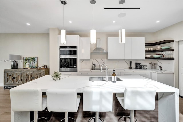 kitchen featuring white cabinets, pendant lighting, a center island with sink, and wall chimney range hood