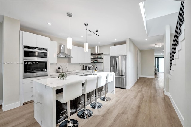 kitchen with pendant lighting, a kitchen island with sink, white cabinets, wall chimney exhaust hood, and stainless steel appliances