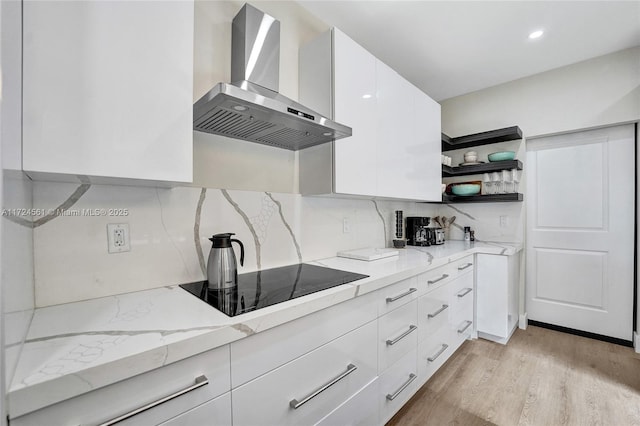 kitchen featuring white cabinetry, wall chimney exhaust hood, light stone counters, backsplash, and black electric stovetop