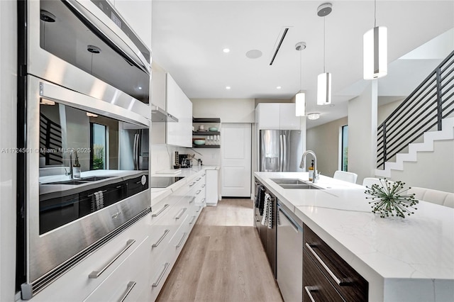 kitchen with sink, hanging light fixtures, stainless steel appliances, a kitchen island with sink, and white cabinets