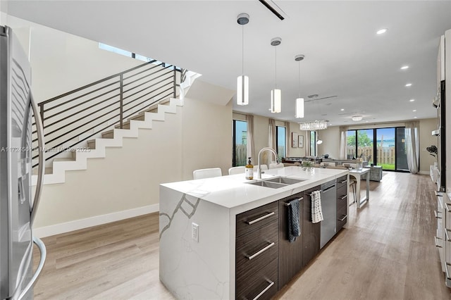 kitchen with sink, dark brown cabinetry, a kitchen island with sink, and light wood-type flooring