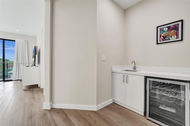 bar with light hardwood / wood-style flooring, white cabinetry, beverage cooler, and sink