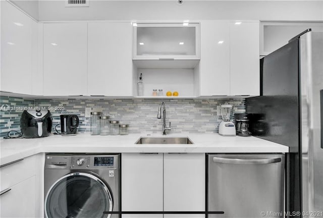 kitchen with backsplash, stainless steel appliances, sink, washer / clothes dryer, and white cabinetry