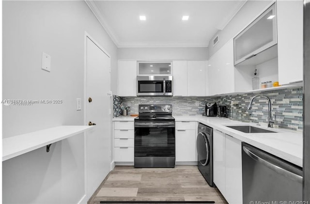 kitchen with appliances with stainless steel finishes, tasteful backsplash, sink, washer / dryer, and white cabinetry