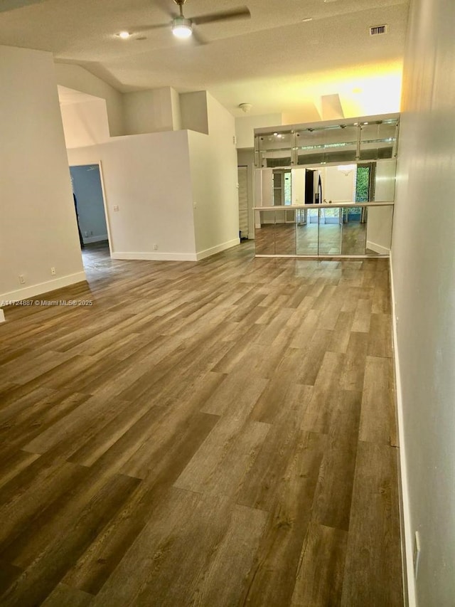 unfurnished living room featuring wood finished floors, a ceiling fan, visible vents, baseboards, and vaulted ceiling