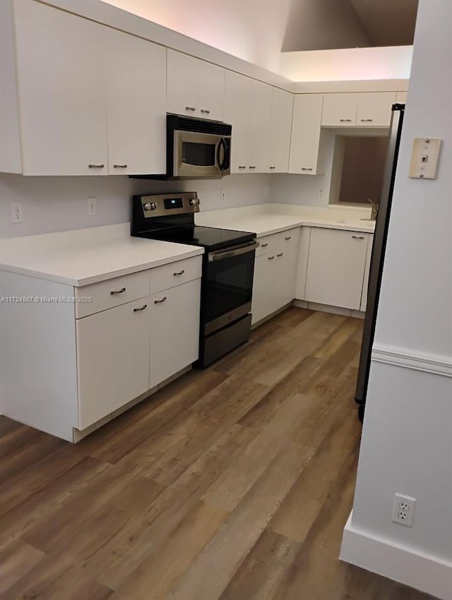 kitchen with appliances with stainless steel finishes, dark hardwood / wood-style flooring, white cabinetry, and lofted ceiling