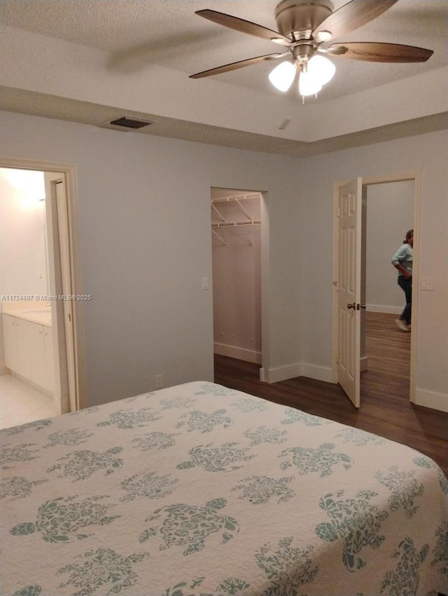 bedroom with a closet, ensuite bath, ceiling fan, dark hardwood / wood-style flooring, and a walk in closet