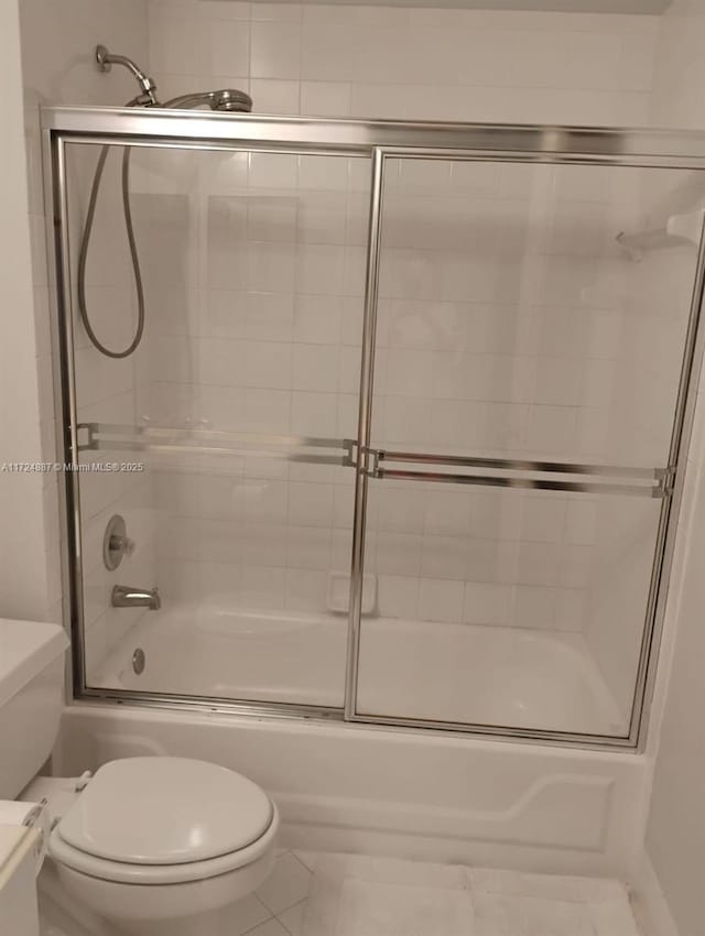 bathroom featuring tile patterned flooring, bath / shower combo with glass door, and toilet