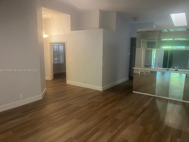 spare room featuring a skylight, baseboards, and dark wood-style flooring