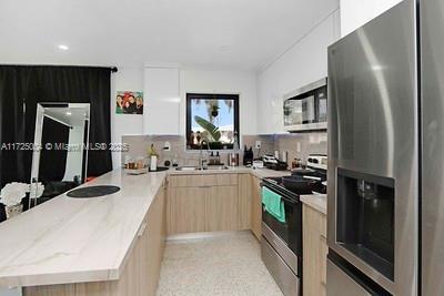 kitchen with light brown cabinetry, light stone counters, stainless steel appliances, sink, and white cabinets