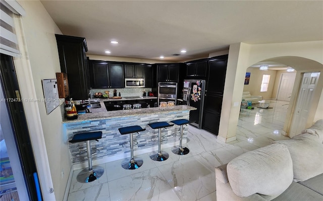 kitchen featuring kitchen peninsula, decorative backsplash, light stone countertops, and black appliances