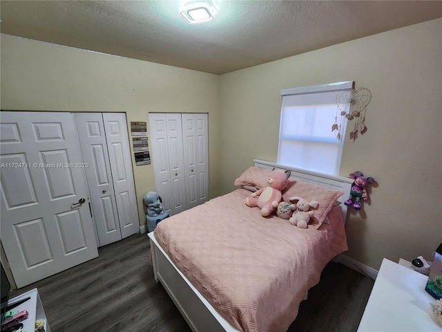 bedroom with a textured ceiling, two closets, and dark hardwood / wood-style floors