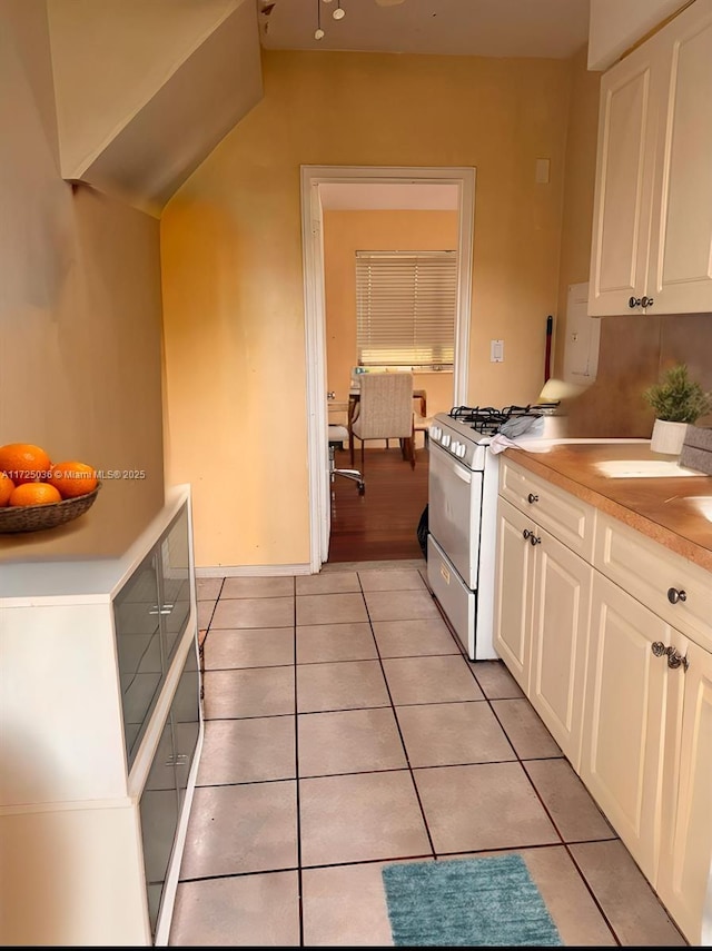 kitchen featuring light tile patterned flooring, white gas stove, and white cabinets