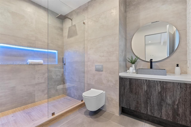 bathroom with a tile shower, tile patterned flooring, toilet, vanity, and tile walls