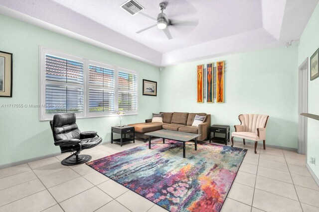 living room featuring a raised ceiling, light tile patterned flooring, and ceiling fan