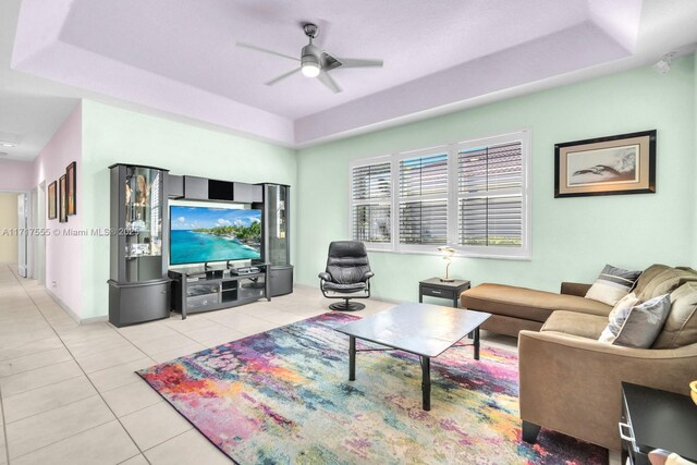 living room with light tile patterned floors, a tray ceiling, and ceiling fan