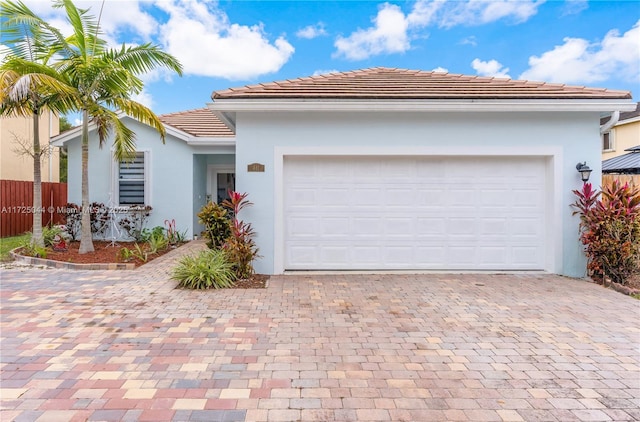 ranch-style house with decorative driveway, a tile roof, stucco siding, fence, and a garage